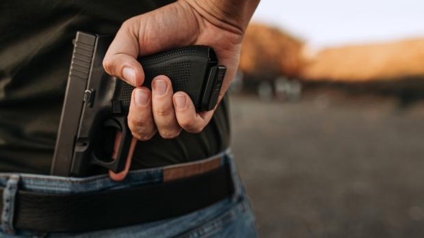 A man holds a gun behind his back as a car approaches