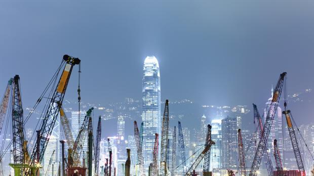 A nighttime view of the Hong Kong skyline with dozens of construction cranes in the foreground and illuminated skyscrapers behind