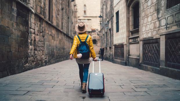 A young woman walks through a Spanish street pulling a suitcase