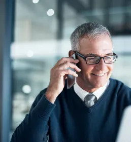 A smiling business man talks on the phone in an open plan office