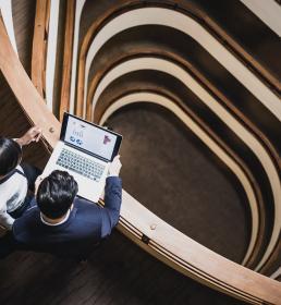 A man and a woman look at financial data on a laptop in the hallway of a modern office