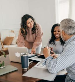 Three colleagues having a friendly discussion around a table with laptops and notebooks in a cozy, modern office