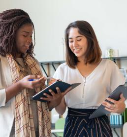 Two professional women smiling and reviewing documents in a modern office