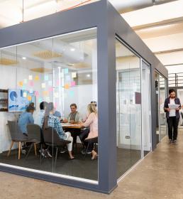 A group of business people sit at a board meeting in a glass-walled room