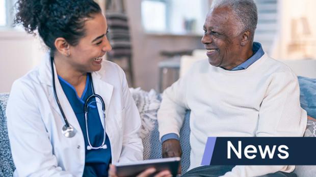 A doctor in a white coat holds a tablet and smiles with her older male patient