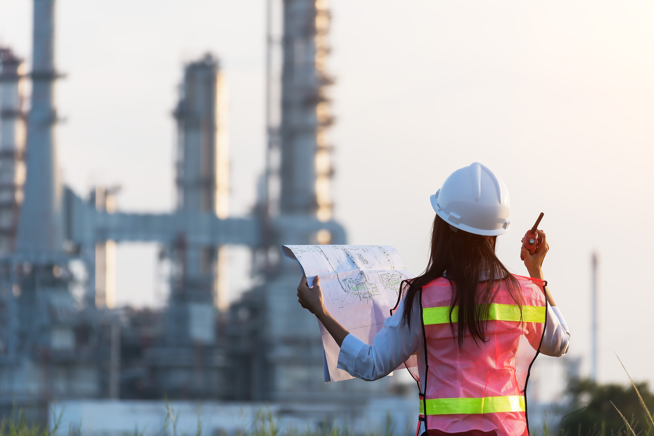 A female engineer holds up blueprints as she surveys a power station from a distance