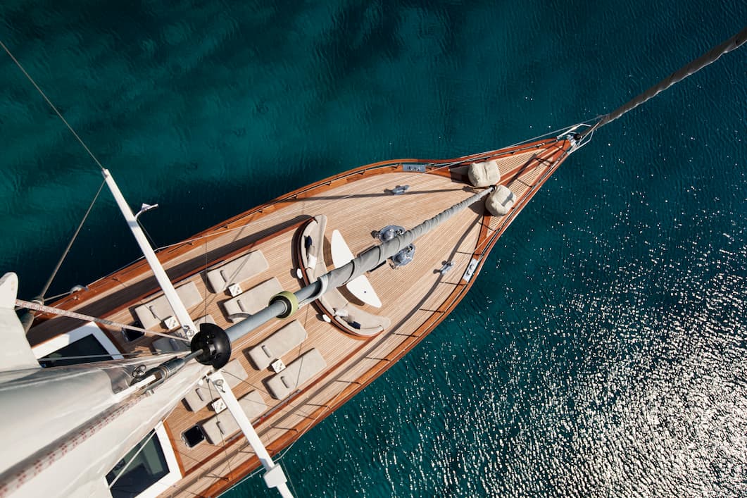 A view from the top of a mast looking down on a luxury yacht sailing in clear waters
