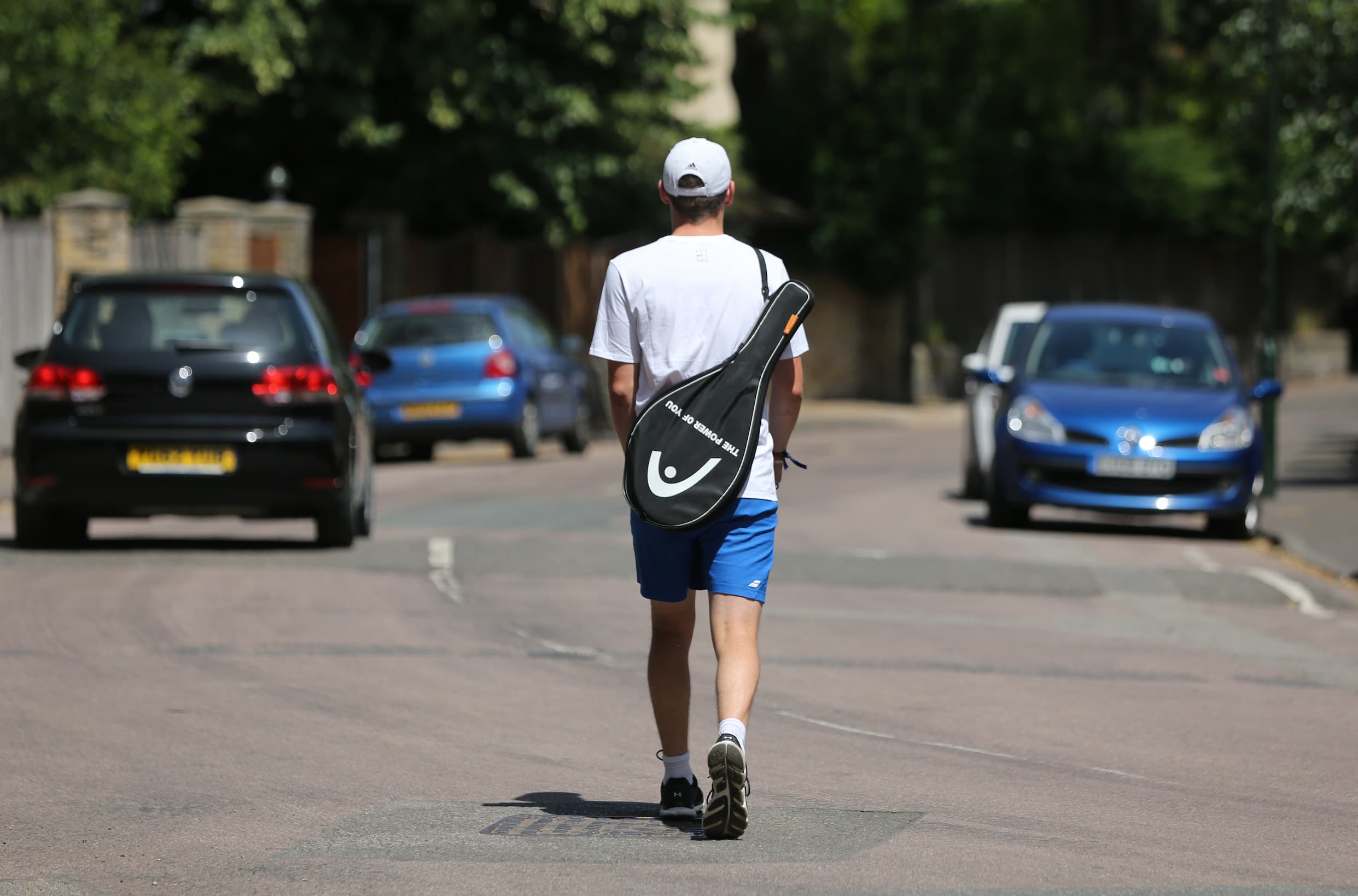 Man with a tennis racquet over his shoulder heading to his car