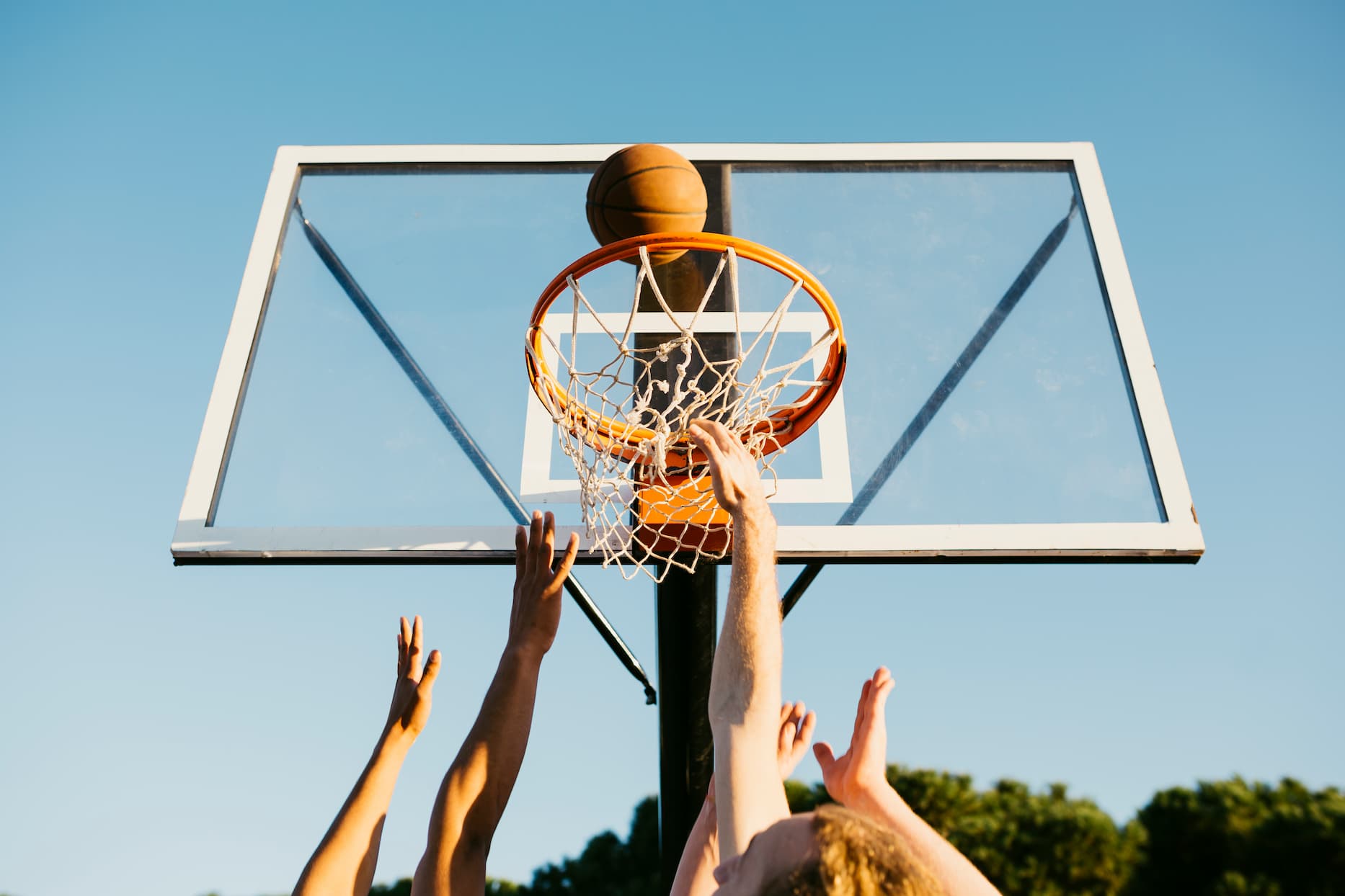 hands reaching towards a basketball hoop and ball