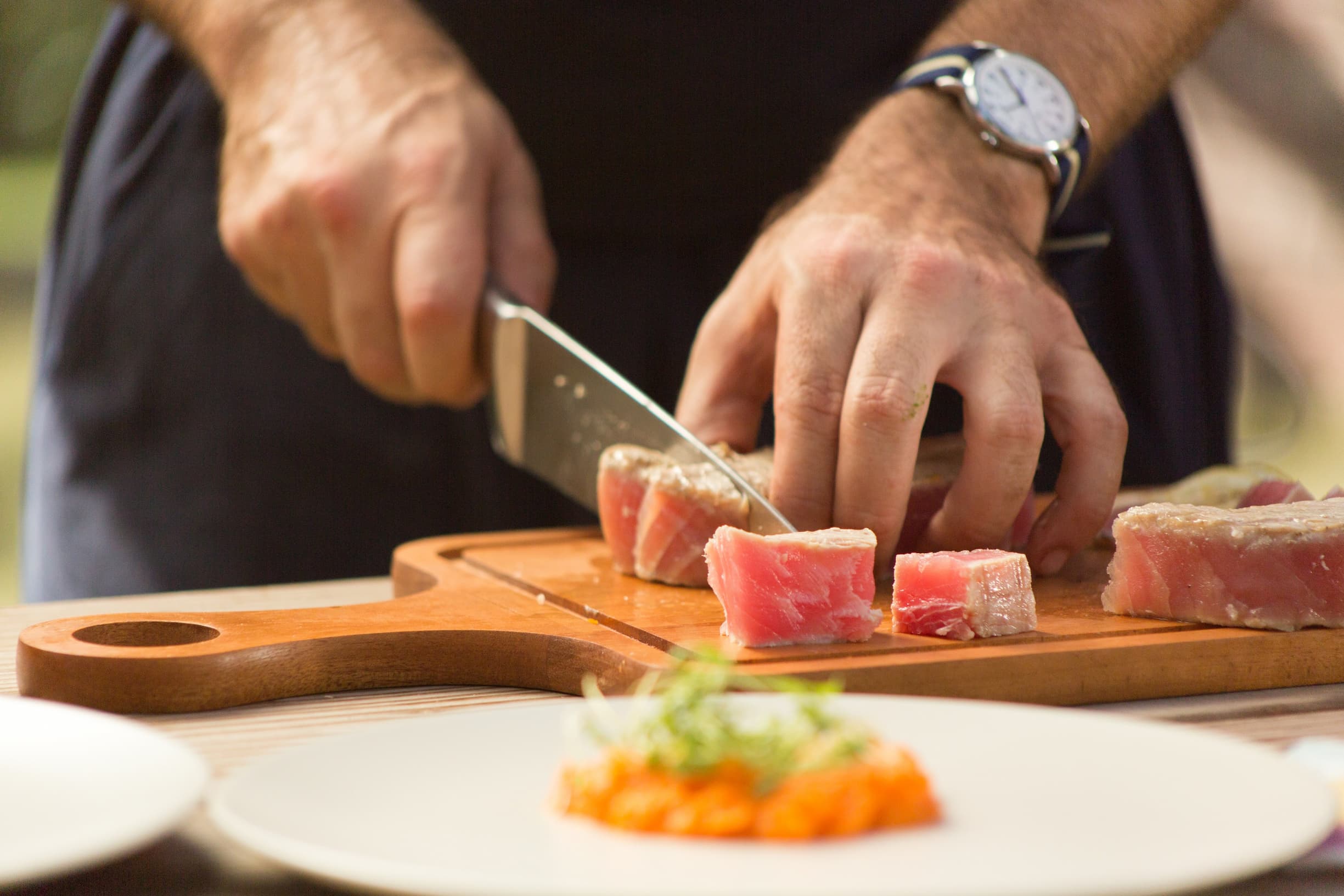 close up of hands chopping fresh tuna on a wooden board