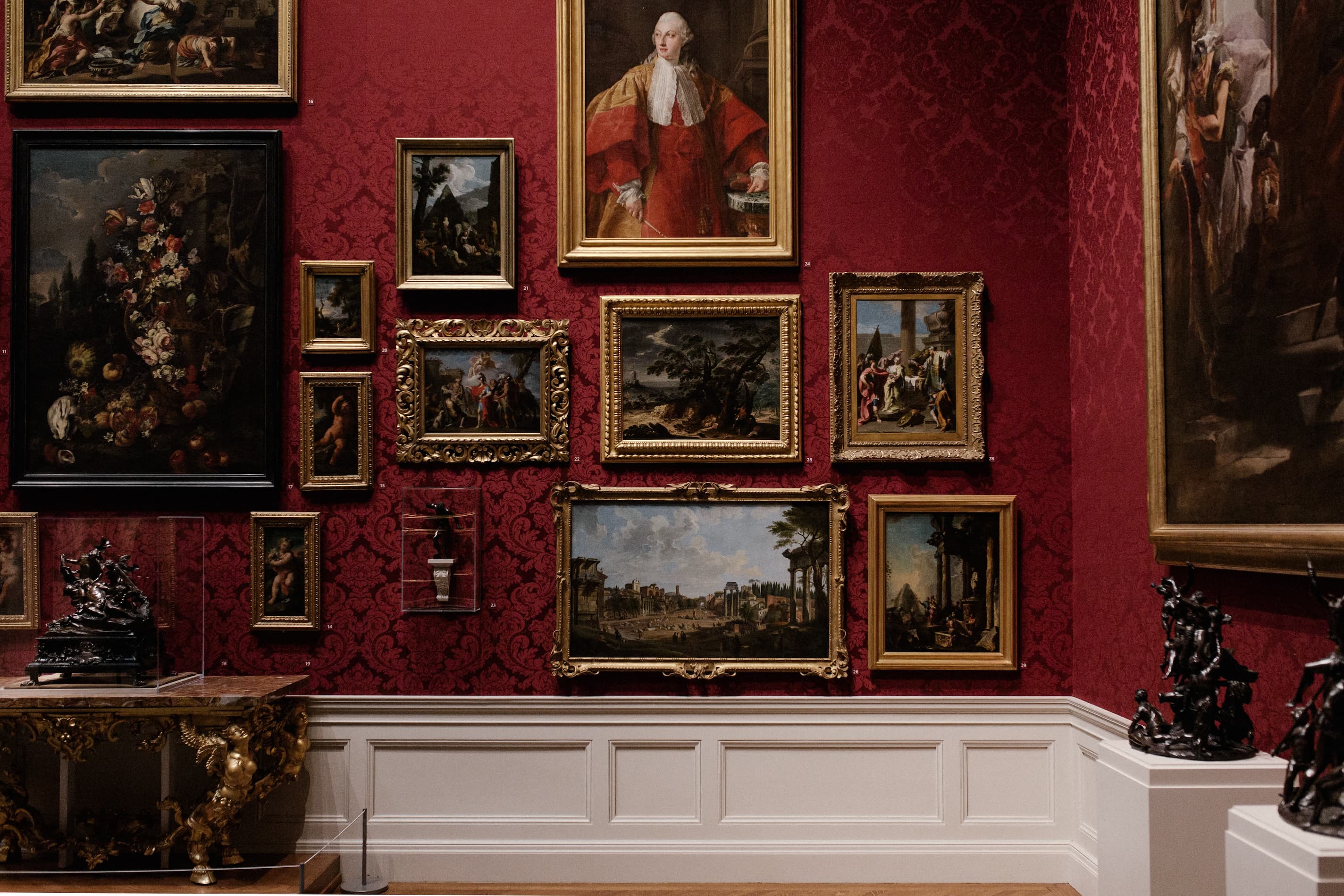 interior of a gallery with framed oil paintings on a red wall