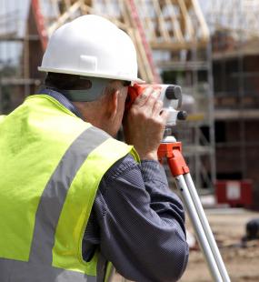 A surveyor looks through a theodolite on a house building site