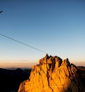 Tightrope walker walking across mountains at dusk