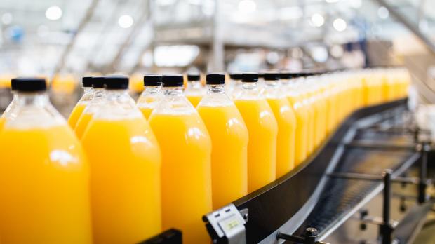 A row of bottles containing orange juice travel along a manufacturing line