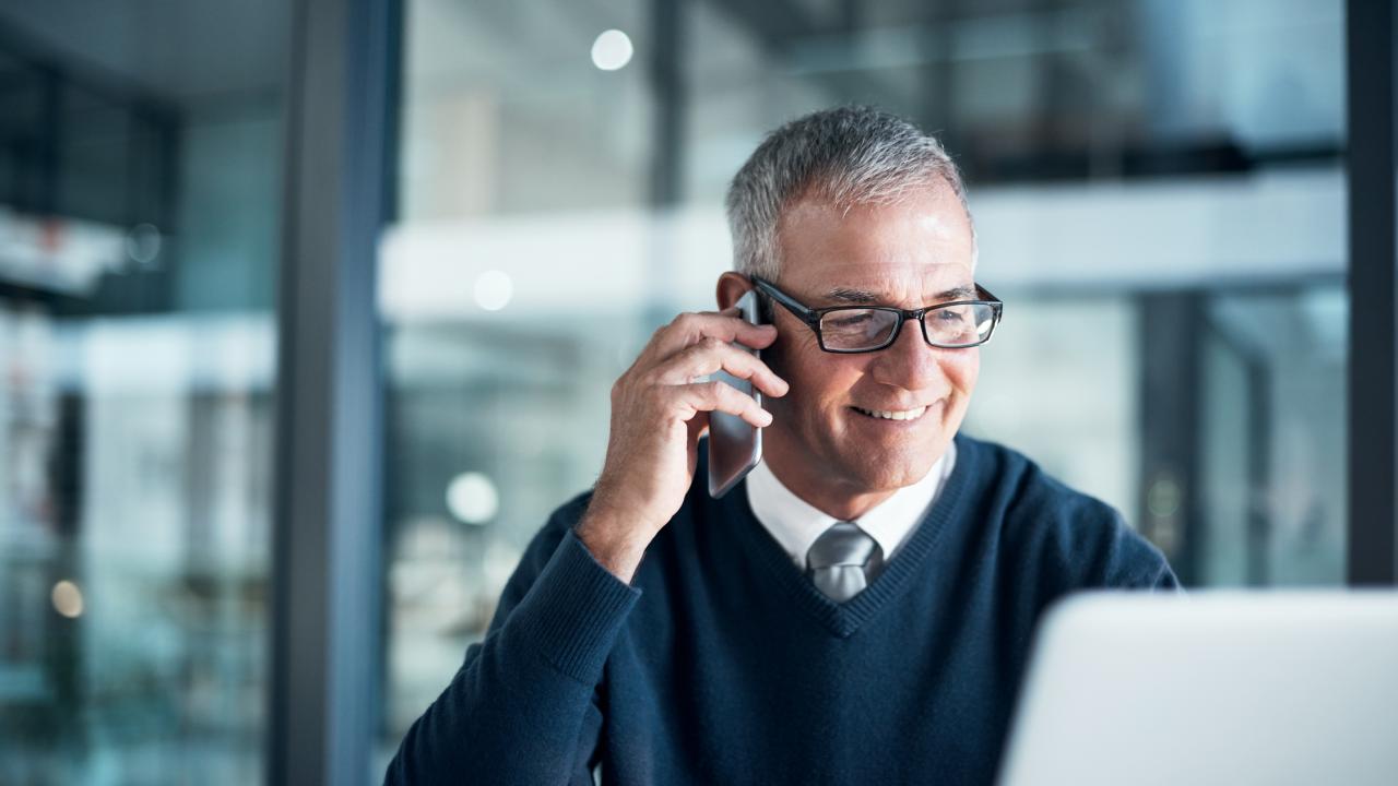 A smiling business man talks on the phone in an open plan office