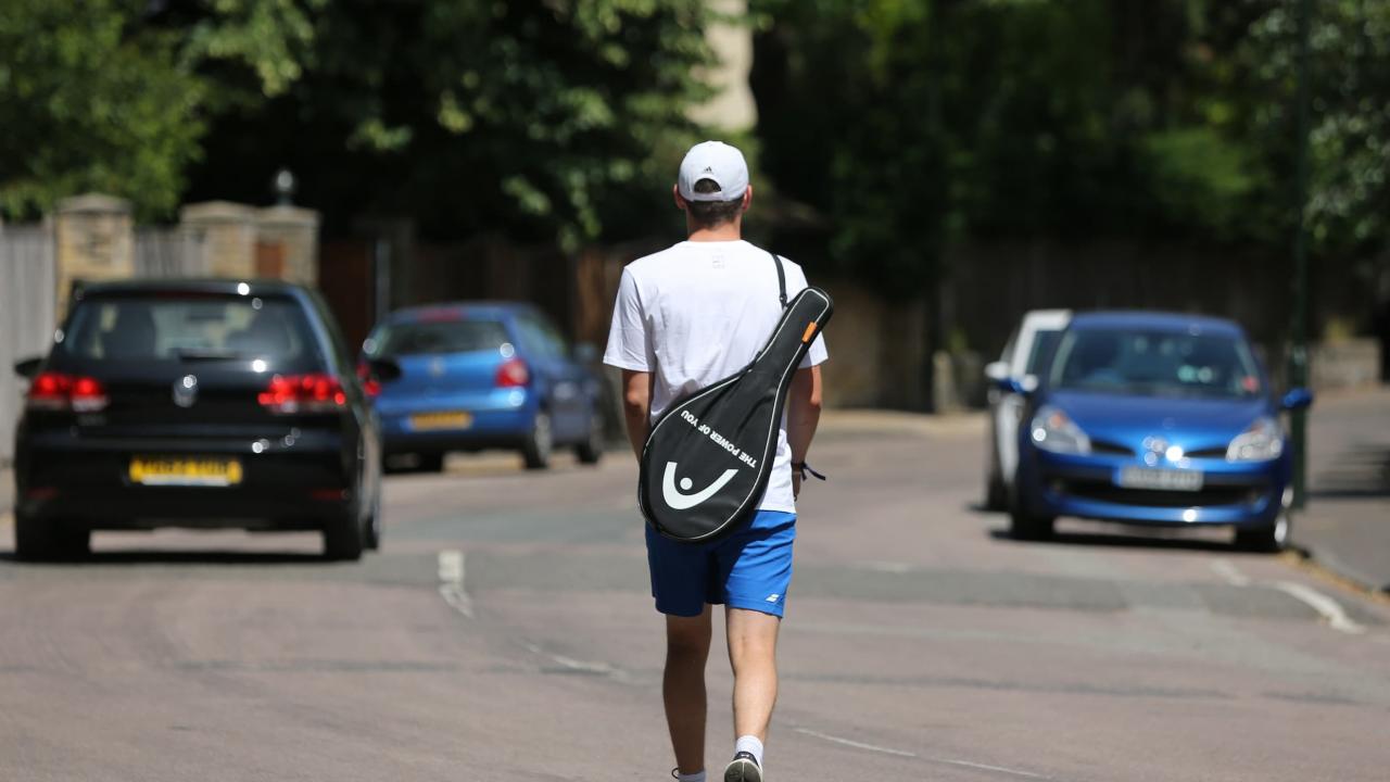 Man with a tennis racquet over his shoulder heading to his car