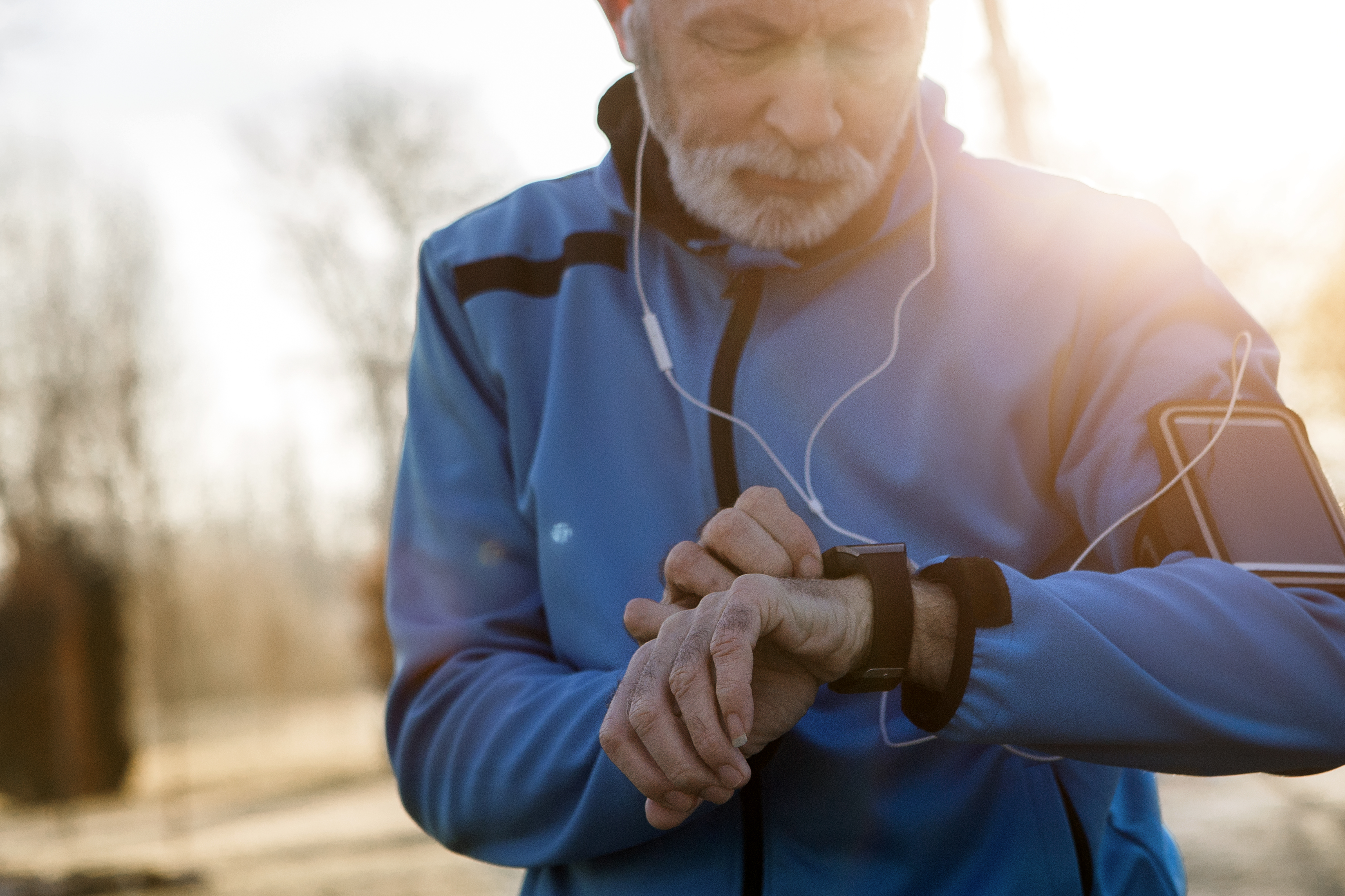 male jogger looking at watch wearing headphones outdoors
