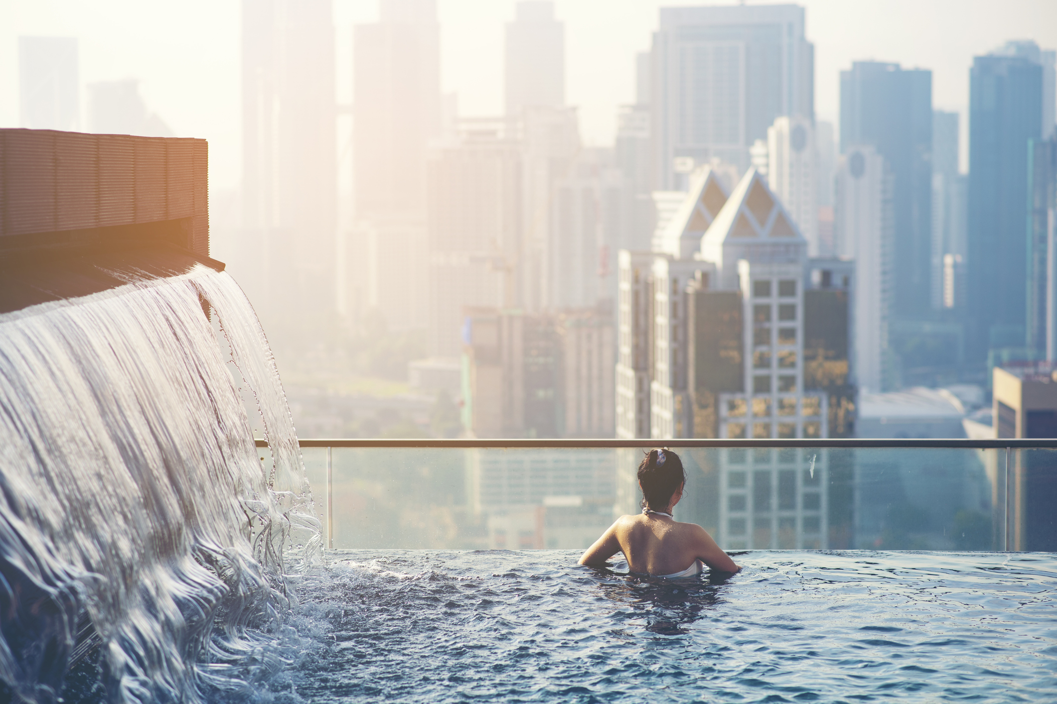 A traveler enjoys the view over the city from a rooftop pool with waterfall