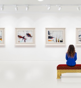 A young woman sits in a gallery admiring the art on the wall