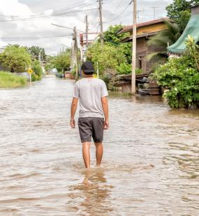 A man walking down a flooded street in Asia - Business interuption