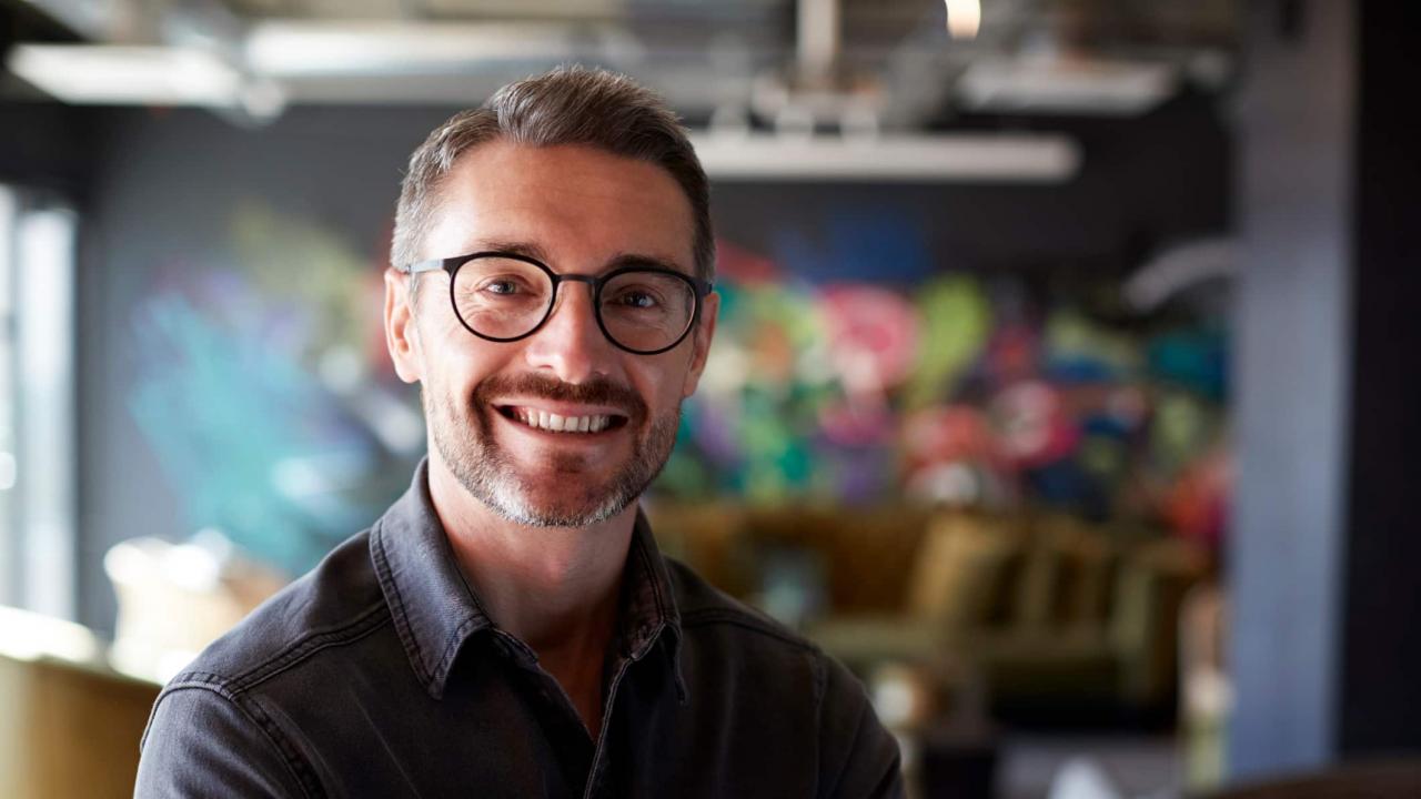A creative businessman stands in a studio smiling at the camera