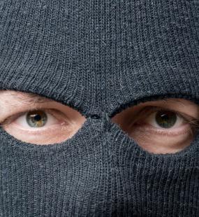 A man in a balaclava looks directly into the camera
