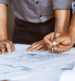 Two planning consultants lean over blueprints laid out on a desk