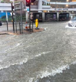 A woman tries to cross a heavily flooded high street as a car drives past in deep water