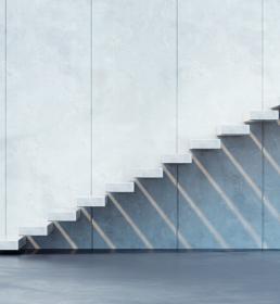 A modern flight of stairs with no riser or banister runs up the side of a building to a platform and casts shadows on the wall below