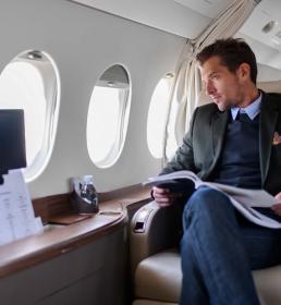 A suave gentleman in a tailored suit looks out of the window of his private jet