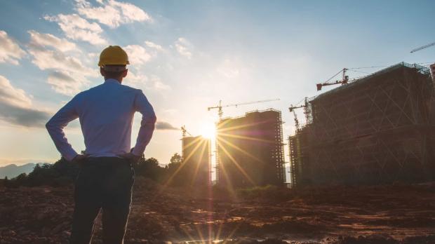 An architect in a shirt and hard hat stands surveying a construction site