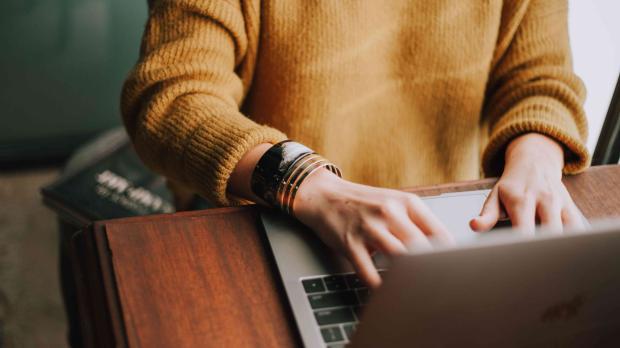 Person in a yellow jumper sat at a desk using a laptop