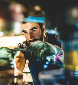 A worker wearing ear protectors and overalls fixes some heavy machinery