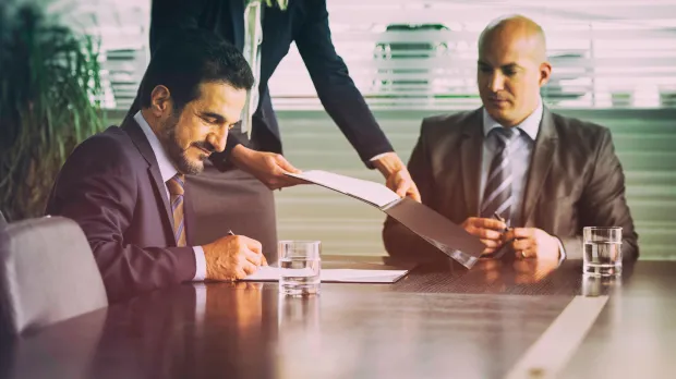 Merger being signed by two guys at a boardroom table