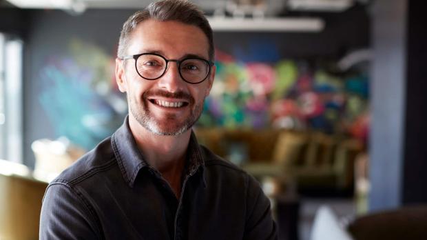 A creative businessman stands in a studio smiling at the camera