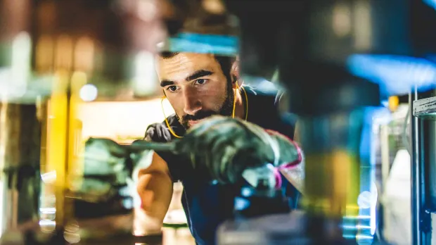 A worker wearing ear protectors and overalls fixes some heavy machinery