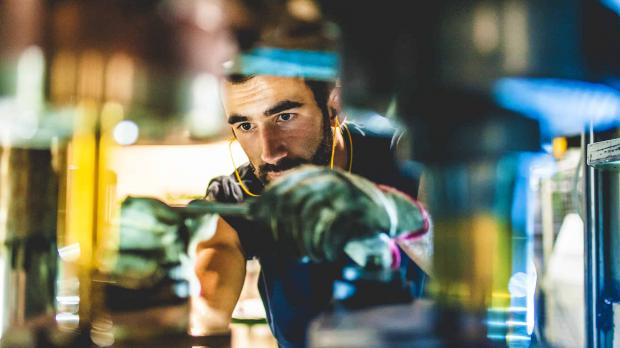 A worker wearing ear protectors and overalls fixes some heavy machinery