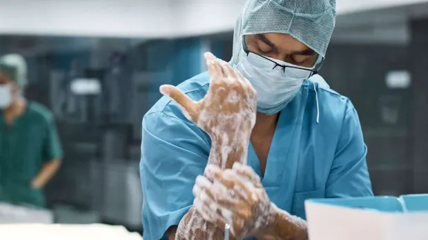 A doctor in scrubs and a face mask washes his hands and wrists in the operating room