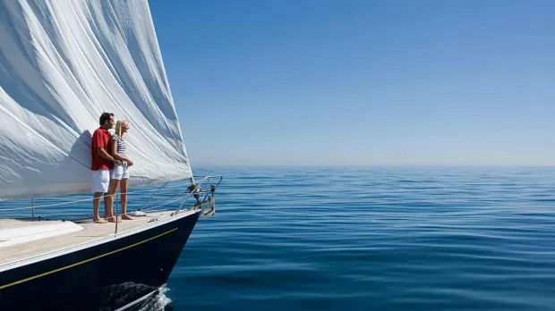A couple stands on their private yacht looking out at the sea