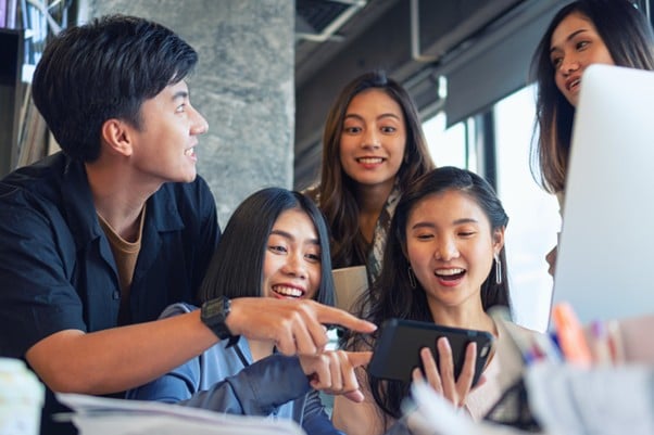 A group of colleagues laughing and interacting with a smartphone in a modern co-working space