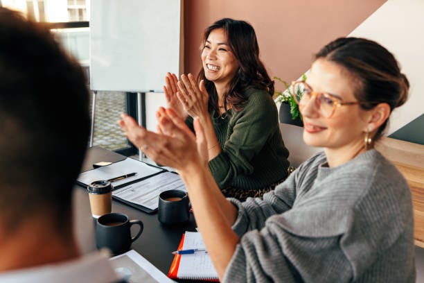 Smiling colleagues applauding during a team meeting in a modern office setting, showing appreciation and positive workplace culture