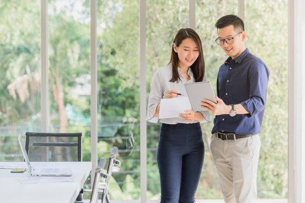Asian coworkers standing in a meeting room discussing a document on a clipboard
