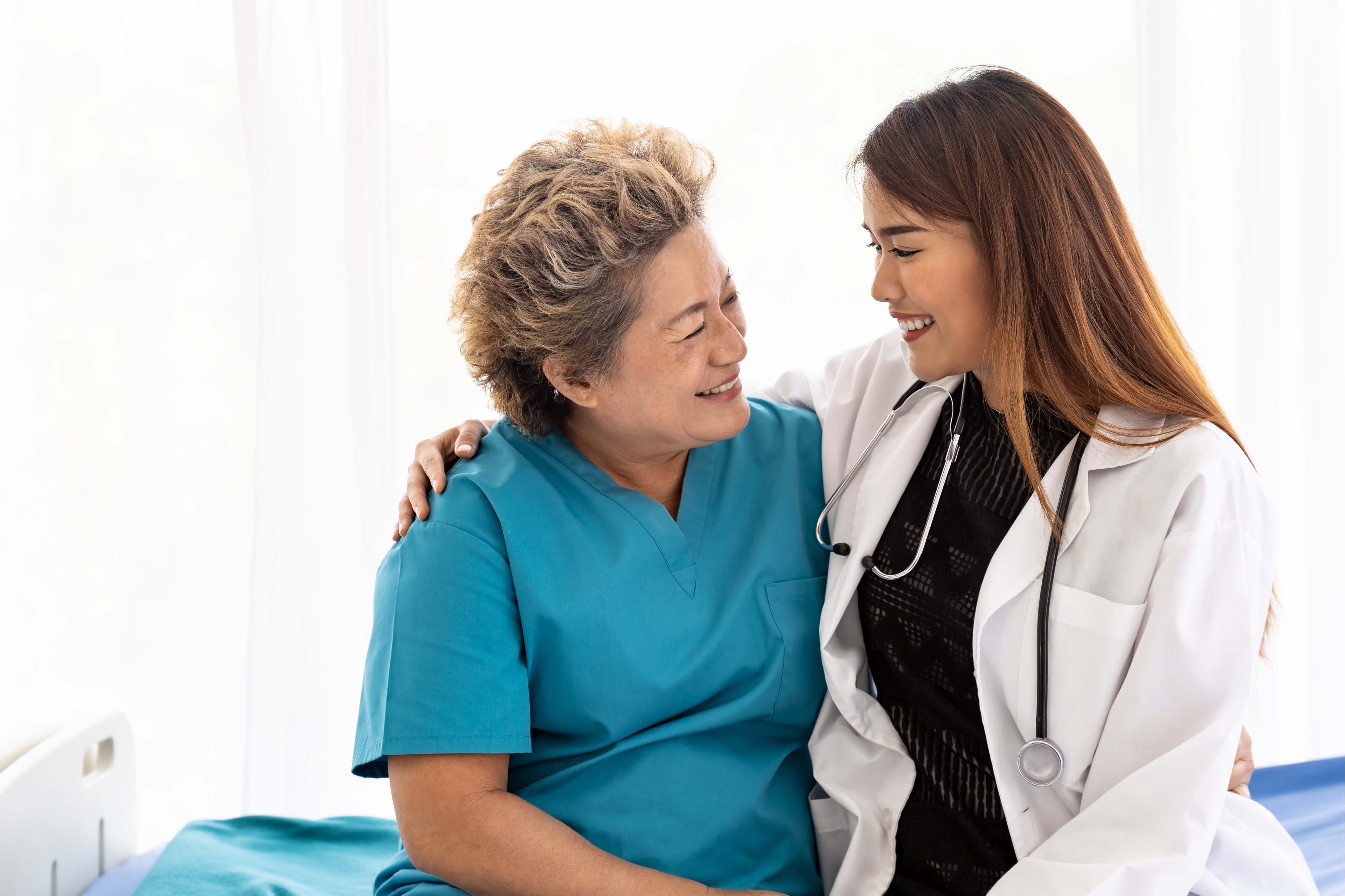 A smiling doctor with a stethoscope embraces an older patient in a Hong Kong hospital, showing warmth and trust.