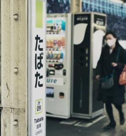 Two young people walk through Tabata Station in Tokyo, wearing face masks