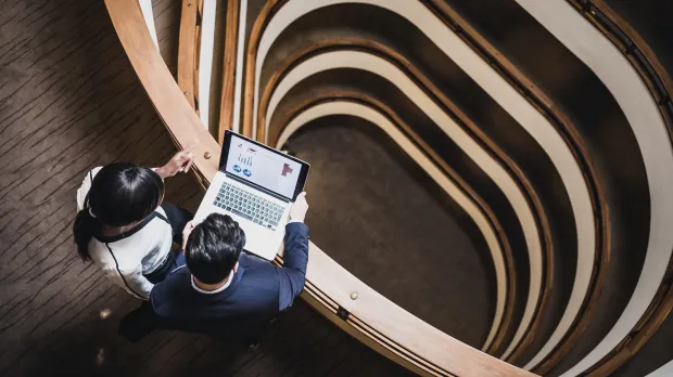 Two finance professionals review accountancy data on a laptop looking out over a spiral staircase