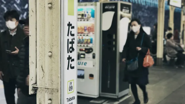 Two young people walk through Tabata Station in Tokyo, wearing face masks