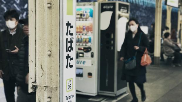 Two young people walk through Tabata Station in Tokyo, wearing face masks