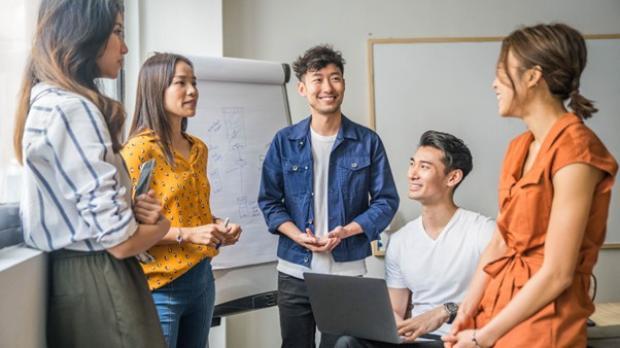 Group of young Asian professionals having a relaxed and cheerful team meeting in a bright modern office