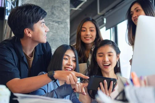 A group of colleagues laughing and interacting with a smartphone in a modern co-working space