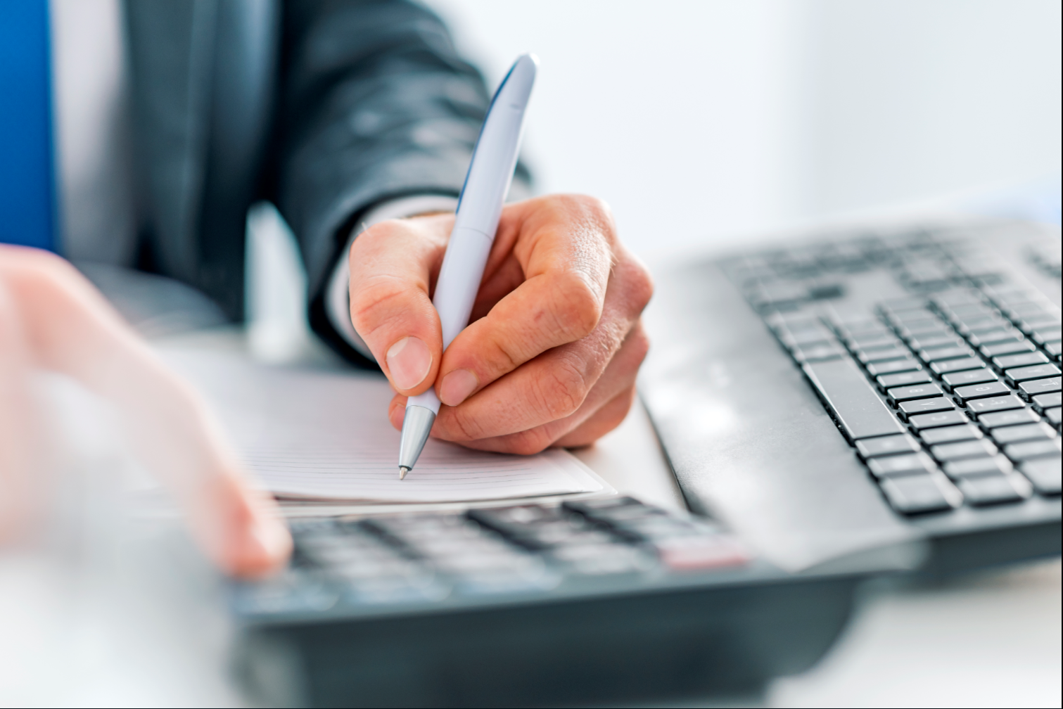 A close-up of a man writing in a notepad